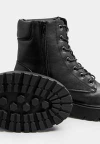 Botas de cuero negro con cierre de cordones en la parte delantera y cremallera lateral. Suela de goma resistente con un patrón de dibujo hexagonal para tracción. Diseño duradero y funcional.