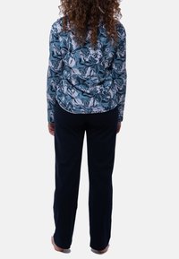 Langærmet blomsterbluse i blå og hvid med en tætsiddende design, parret med mørkeblå, løstsiddende bukser. Glat tekstur, ingen synlige mønstre på bukserne.