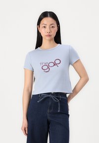 Camiseta cortada de color azul claro, hecha de algodón suave, con mangas cortas y escote redondo, que presenta un logo burdeos de "the gap" en el centro.