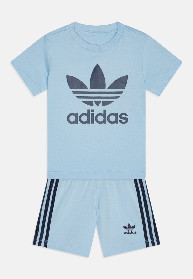 Svetlomodrý Adidas dvojdielny set, ktorý obsahuje tričko s tmavomodrým logom a zodpovedajúce šortky s námorníckymi bočnými pruhmi a akcentmi loga.