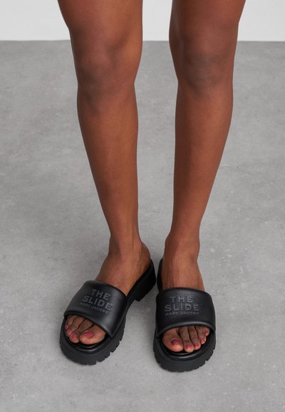 Svarte sandalene med bred såle har en teksturert stropp og tykk gummisåle. Har preget tekst "THE SLIDE MARC JACOBS" på stroppen.