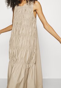 Robe sans manches beige avec texture froncée, encolure ronde et coupe ample. Design froncé distinctif sur toute la longueur, silhouette fluide.