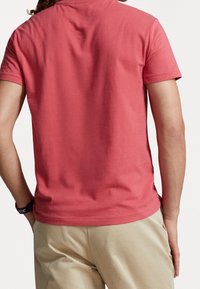 Kortärmad korallfärgad t-shirt i bomull med rund halsringning och mjukt tyg, kombinerad med beige byxor.