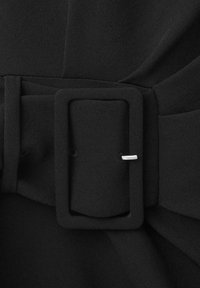 Gros plan d'une ceinture en tissu noire avec une boucle rectangulaire recouverte et une petite ardillon argentée visible fixant la ceinture.