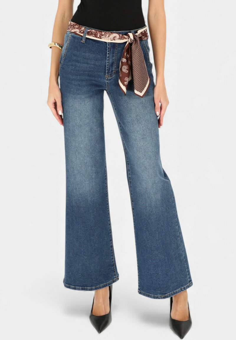 Niebieskie dżinsy o szerokich nogawkach z brązowym paskiem w wzory i przeszyciami, zestawione z czarnymi szpilkami z ostrym noskiem.