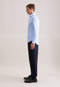 Camicia azzurra a maniche lunghe con colletto a punta, abbinata a pantaloni blu scuro e scarpe nere. Tessuto liscio e vestibilità sartoriale.