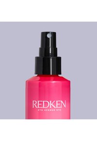 Redken haarproduct in een gradient roze fles met een zwarte spraymond. Bevat witte tekst "REDKEN" en "5TH AVENUE NYC." Glad, glanzend oppervlak.