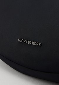 Černá nylonová taška přes rameno s elegantním designem, texturovaným povrchem a stříbrnou kovovou logem "MICHAEL KORS".