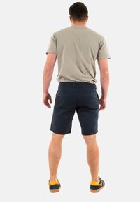 T-shirt gris et short marine avec deux poches arrière, porté par une personne de dos. Les chaussures présentent des accents jaunes et une semelle sombre.