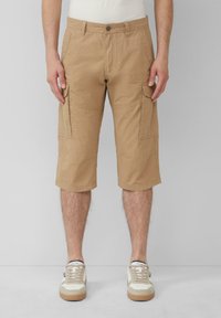 Beige Cargo-Shorts aus strukturiertem Stoff, ausgestattet mit seitlichen Taschen, einem Knopfverschluss und taillierter Passform, kombiniert mit beigen Sneakers.