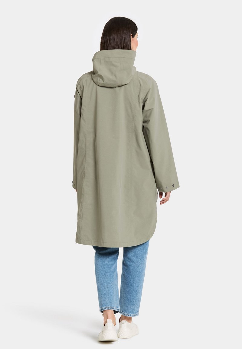 Hellgrüner, übergroßer Regenmantel mit Kapuze, langen Ärmeln und Druckknopfverschlüssen; kombiniert mit blauen Jeans und weißen Slippern.