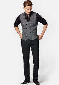 Szary kamizelka w kratę noszona na czarnej koszuli, w połączeniu z czarnymi spodniami i czarnymi trampkami. Kamizelka ma podwójne zapięcie i teksturowany materiał.