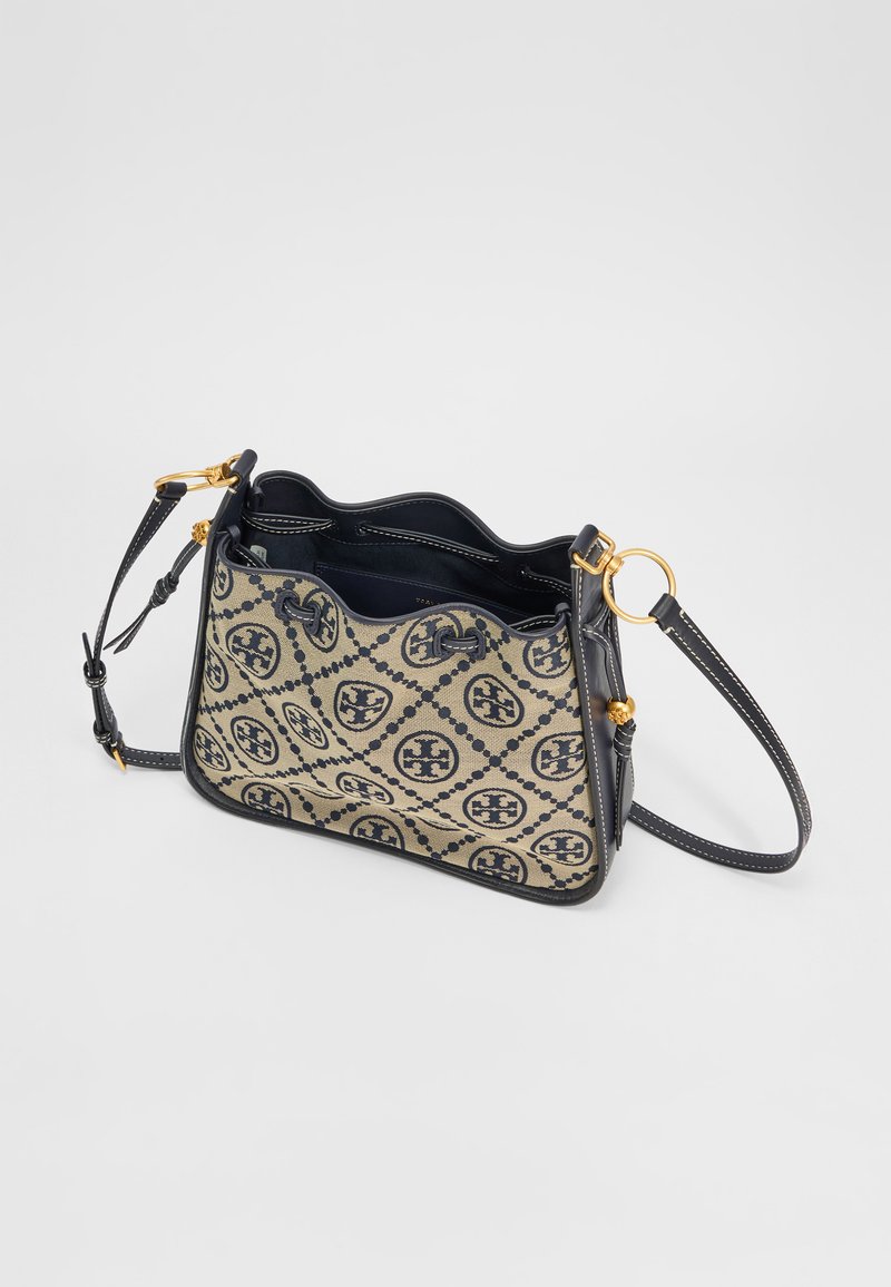 Texturiertes Canvas-Handtasche in Beige mit Navy-Muster, ausgestattet mit goldfarbenen Beschlägen und einem gebogenen oberen Teil. Verstellbarer Ledertrageriemen für vielseitige Verwendung.