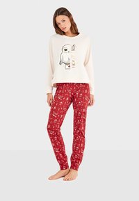 Haut à manches longues crème avec un graphique de hibou et le texte "HOGWARTS", associé à un pantalon de pyjama rouge avec des motifs blancs fantaisistes. Tissu doux.