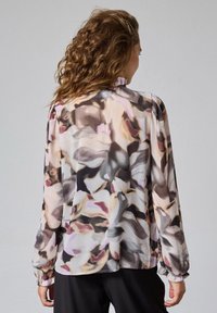 Let og langærmet bluse i gennemsigtigt stof med et flerfarvet blomstermønster i nuancer af pink, grå og creme. Har en samlet manchet.