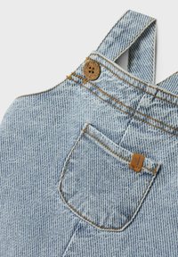 Svetlomodré denimmové nohavice s nastaviteľnými popruhmi, malou vrecko a kontrastným oranžovým prešívaním. Obsahuje detail zaobleného dreveného gombíka.