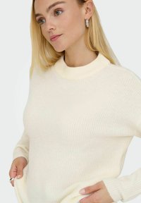 Cremfarbener gerippter Pullover mit hohem Kragen und langen Ärmeln. Weicher Stoff mit lockerer Passform. Einfaches, funktionales Design.