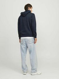 Sudadera azul marino con capucha ajustable, combinada con jeans de corte holgado en azul claro. El conjunto se complementa con zapatillas blancas.