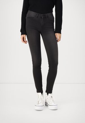 Zwarte skinny jeans met een gladde textuur, hoge taille, vijf zakken en riemlussen, gecombineerd met witte hoge sneakers.