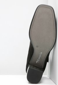 Czarny zamszowy but z zaokrąglonym noskiem, teksturowaną podeszwą i szaro-rubberowym spodem. Posiada subtelne oznaczenia marki i rozmiaru na spodzie.