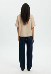 Un haut beige à manches courtes en matière douce, associé à un jean large à taille haute bleu foncé, mettant en valeur une silhouette droite.