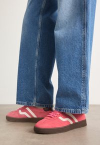 Rosa semskesneakers med hvite bølgete striper og brune gummisåler, kombinert med lys blå vide denimjeans.