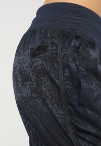 Námořnické sportovní kalhoty s texturovaným vzorem, elastickým pasem, boční kapsou a černým logem Nike na zadní straně.