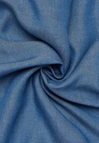 Jeansstoff in Mittelblau mit glatter Textur, präsentiert in einer wirbelnden Faltung, zeigt ein dezentes Köpermuster und klare Kanten.