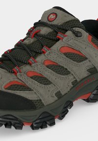 Chaussure de randonnée avec suède gris et mesh, détails noirs et rouges, lacets noirs à motifs, semelle noire robuste, marque Merrell sur le côté.