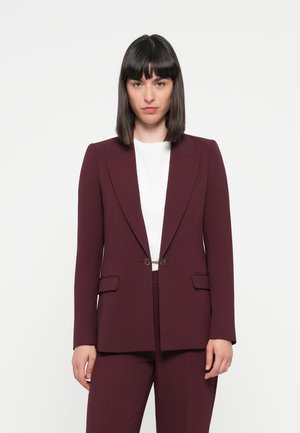 Blazer tailored color bordeaux con finitura satinata, rever a punta e dettagli in oro. Presenta due tasche frontali e chiusura con un solo bottone.