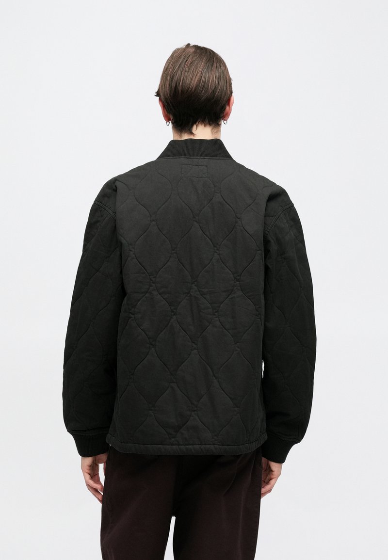 Black quilted bomber jacket with a ribbed collar and cuffs, featuring a textured pattern and a relaxed fit. No visible branding.