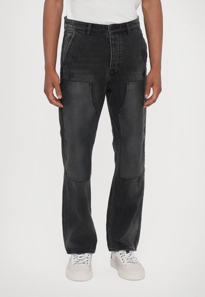 Black denim pants featuring leather panels on the front, loose fit, straight leg design, and stitched detailing. Paired with white sneakers.