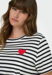 Stripet T-skjorte i hvit og marineblå, med en teksturert rød hjerteapplikasjon på brystet. Korte ermer og rund halslinning. Mykt stoff.