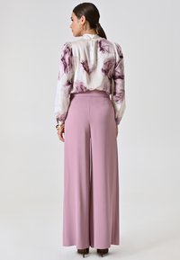 Blusa di seta con stampa floreale in lavanda su sfondo bianco, abbinata a pantaloni palazzo a vita alta in rosa morbido. Tessuto liscio, vestibilità elegante.