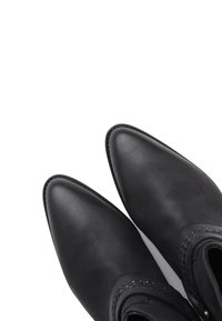 Paire de bottes en cuir noires à bout pointu avec coutures décoratives près de la cheville, photographiées en plongée sur un fond blanc.