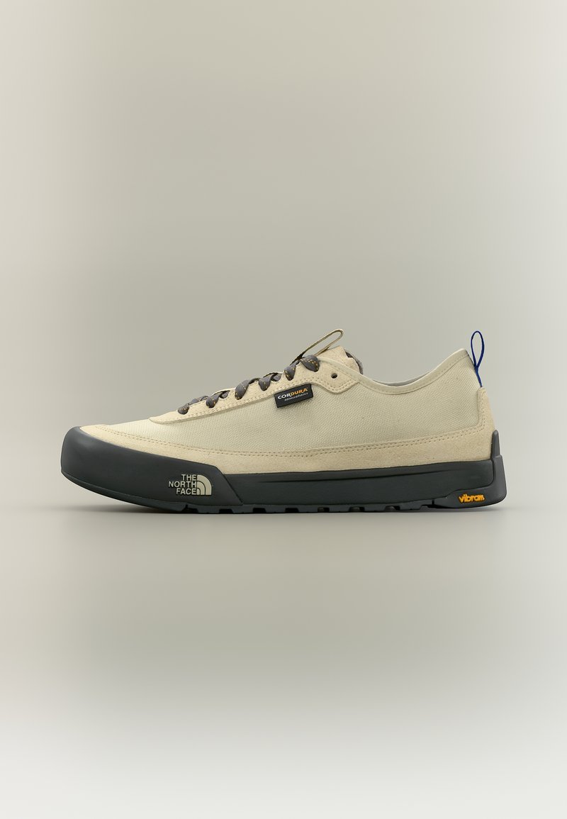 Μπέζ sneaker χαμηλού πάτου με μαύρη καουτσούκ σόλα, μαύρο κάλυμμα στα δάχτυλα, σκούρα κορδόνια, μπλε θηλιά στη φτέρνα και λογότυπα από The North Face και Vibram.