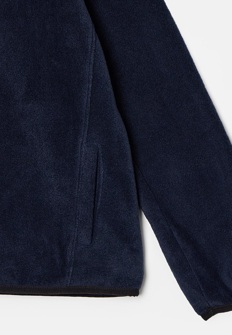 Veste en polaire bleu marine avec une texture douce, dotée d'une poche latérale et d'une finition noire le long de l'ourlet et des poignets.