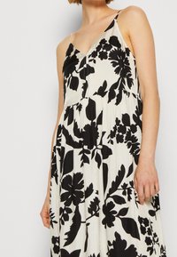 Svart och vit blommig klänning med v-ringning, tunna axelband och lätt tyg med plisseringar vid midjan för en svepande silhuett.