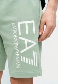 Ανοιχτό πράσινο βαμβακερό σορτς με μεγάλα λευκά τυπωμένα λογότυπα, «EA» και «EMPORIO ARMANI», με άνετη εφαρμογή και ίσιο τελείωμα.