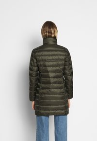 Olive green puffer coat with a high collar, quilted design, and long silhouette, paired with light blue wide-leg jeans.