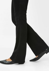 I jeans neri a zampa d'elefante presentano una texture liscia e un design classico, abbinati a ballerine nere con punta e un sottile dettaglio di cucitura.