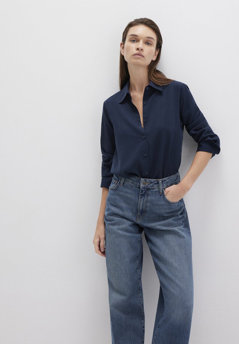Navy button-up shirt with rolled sleeves paired with high-waisted light blue jeans, featuring a relaxed fit and straight leg cut.