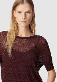 Bordeaux gebreide trui met een ruitpatroon, korte mouwen en een wijde hals, voorzien van een doorzichtige textuur en ribgebreide manchetten.