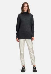 Un pull noir pailleté avec un col montant et des poignets côtelés, associé à un pantalon lumineux de couleur claire et des chaussures noires épaisses.