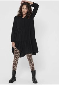 Melnā, slāņota kleita ar pogātu apkakli, kombinēta ar leopardu raksta legingiem un melniem potīšu zābakiem. Gluda auduma un brīva piegriezuma.