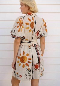 Kurzärmliges, beiges Kleid mit floralen und Sonnenmustern in Orange und Schwarz. Mit einem taillierten Bund und einem strukturierten, leichten Stoff.