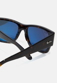 Ochelari de soare cu rame din material tartan și lentile albastre. Design unghiular și finisaj lucios. Prezintă branding-ul Ray-Ban pe tâmple.