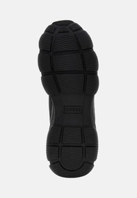 Black sneaker sole with textured patterns, prominent ridges, and rubber material. Features brand logo "GUESS" embossed in the center.