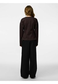 Smeđa uska majica s dugim rukavima uparena s visokim strukom i širokim nogavicama crnih hlača s tankim prugama, prikazana s leđa.