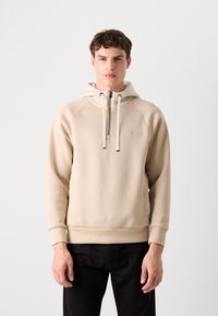 Haut à capuche beige avec un col zippé, une capuche avec cordon de serrage et des poignets côtelés. Texture lisse avec un motif de logo discret sur la poitrine.